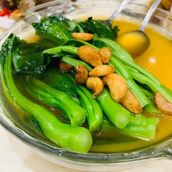 Steamed green Chinese vegetables with fried garlic cloves in a clear bowl with a golden broth.