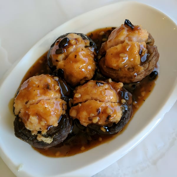Four Chinese stuffed mushrooms with a savory brown sauce on a white plate.