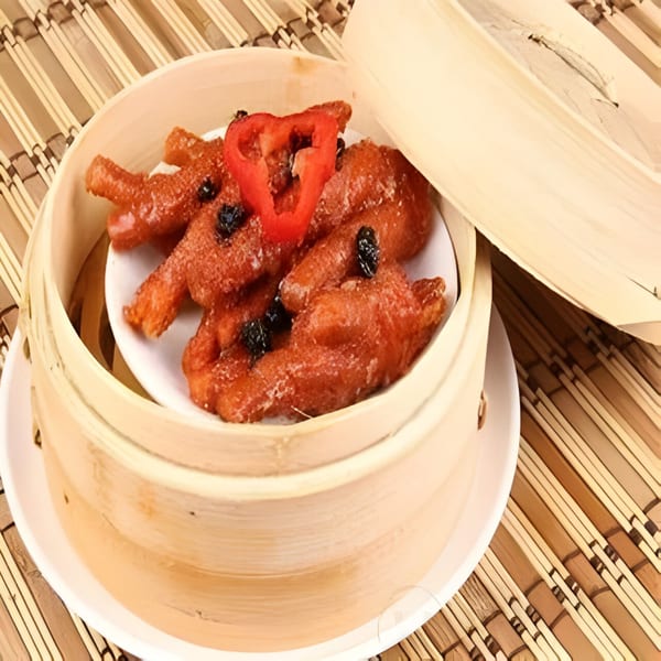 Steamed chicken feet with red pepper and black beans in a bamboo dim sum basket.