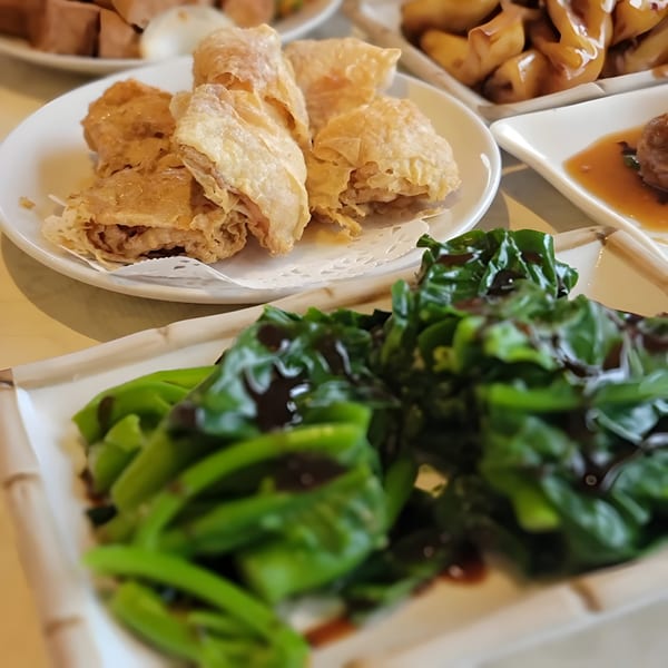 Plates of crispy fried bean curd skin rolls and vibrant green Chinese broccoli with oyster sauce.
