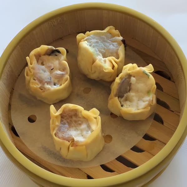 Four steamed Chinese shumai dumplings with white filling in a bamboo steamer.