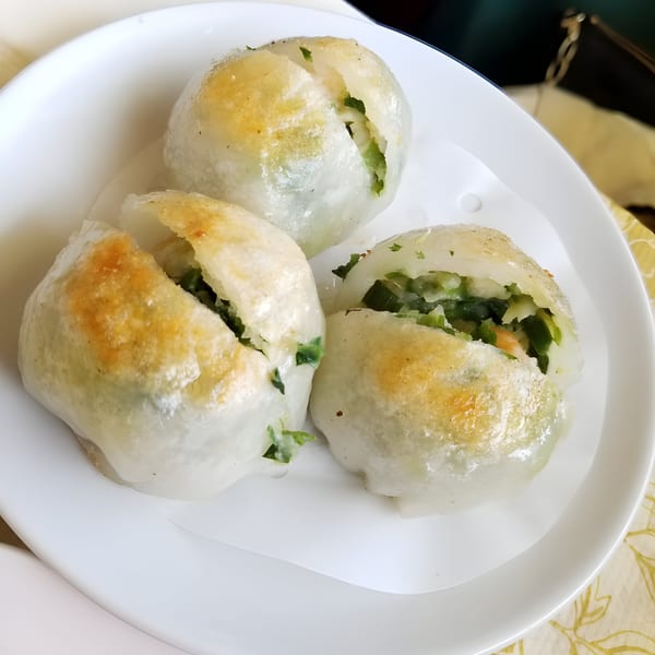 Three pan-fried Chinese chive dumplings with golden-brown tops and green filling visible on a white plate.